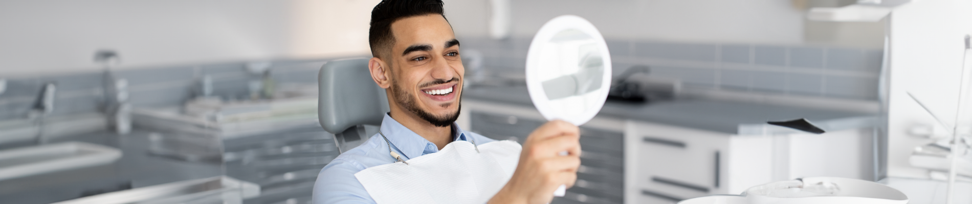 Man in the dental chair checking his smile in a handheld mirror