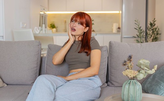 Woman experiencing jaw pain while she sits on sofa