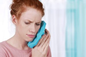 Woman holding cold compress to her face experiencing pain.